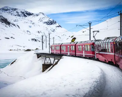 Bernina Express train, one of the highest railway in the world, goes across a little bridge in snowy mountain near a frozen lake