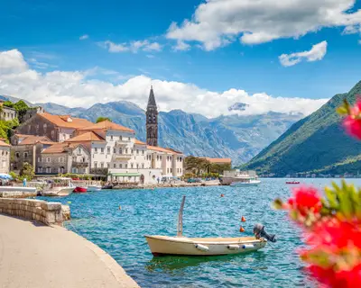 Scenic panorama view of the historic town of Perast at famous Bay of Kotor with blooming flowers on a beautiful sunny day with blue sky and clouds in summer, Montenegro, southern Europe