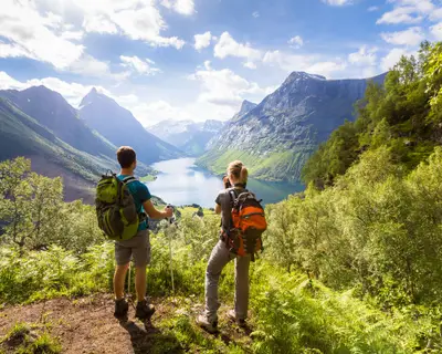 Two hikers at viewpoint in the mountains enjoying beautiful view of the valley with a lake and sunny warm weather in summer, green trees around