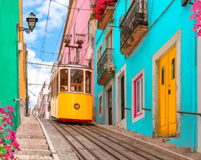 Yellow electric tram on a street with colorful houses and flowers on the balconies - Bica Elevator going down the hill of Chiado in Lisbon, Portugal.