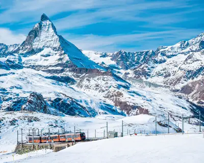 View of red train climbing up to gornergrat station. Scenic view of matterhorn mountain against sky. Famous tourist place in alpine region.